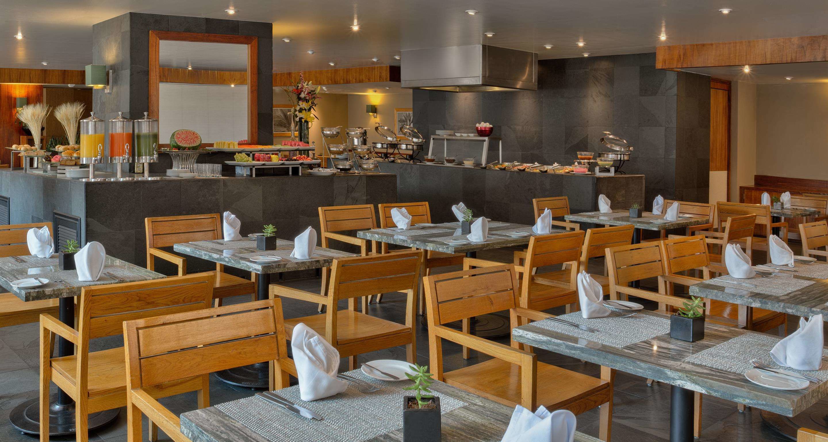 A restaurant with multiple tables and chairs, a buffet area with various food items, and a modern interior design.