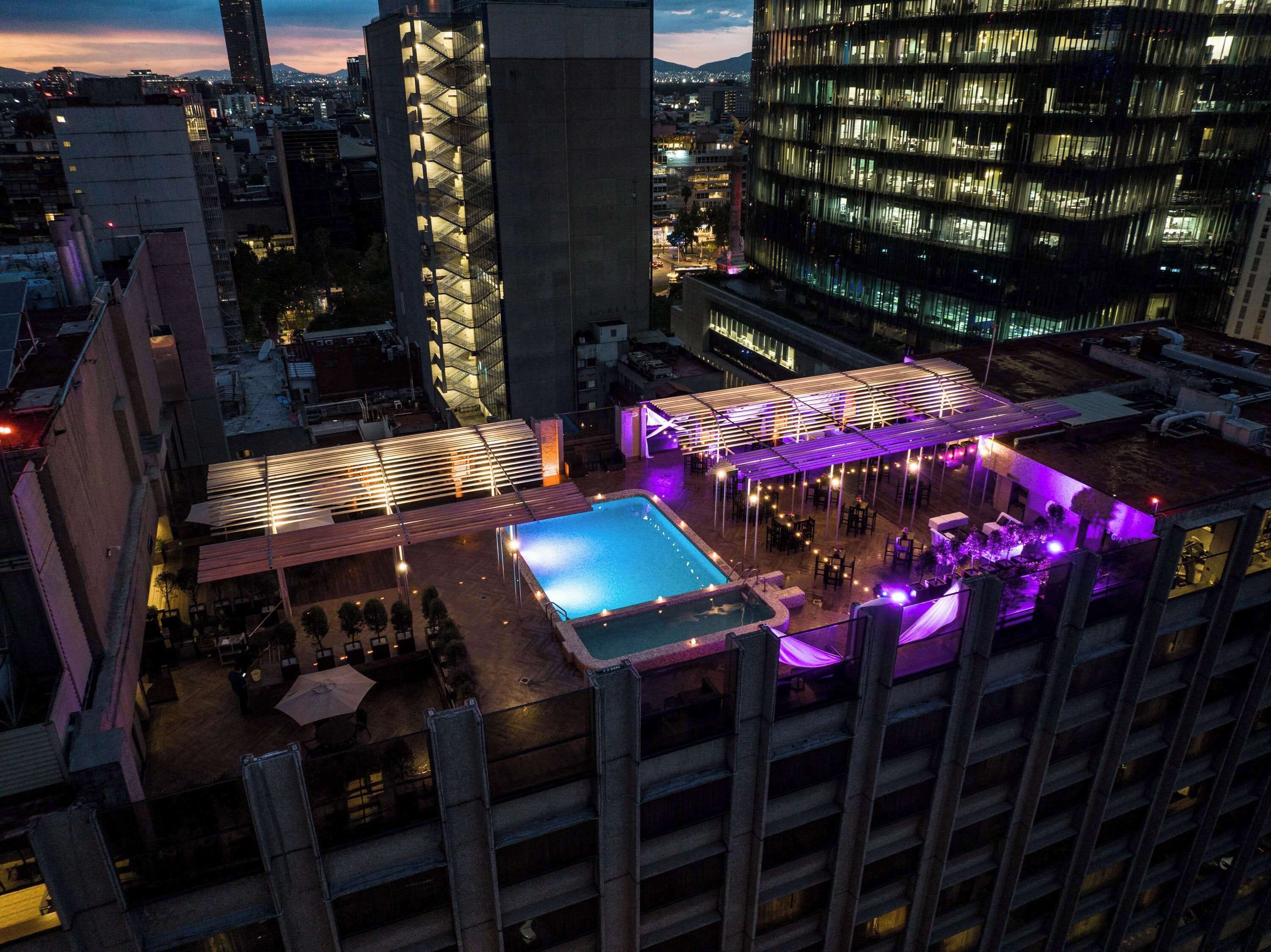 A rooftop pool area with a glass enclosure, surrounded by outdoor seating and a covered patio.
