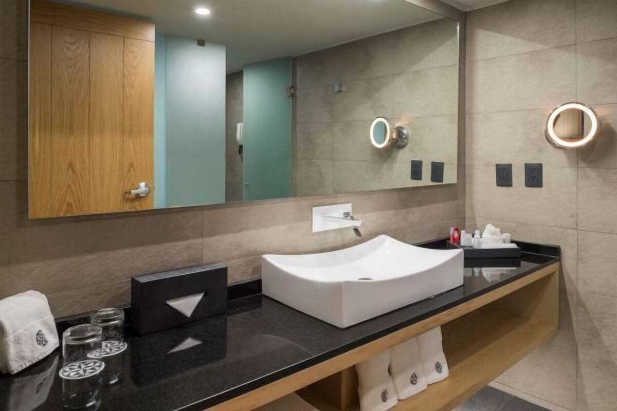 A modern bathroom with a large mirror, a white sink, and a wooden vanity.