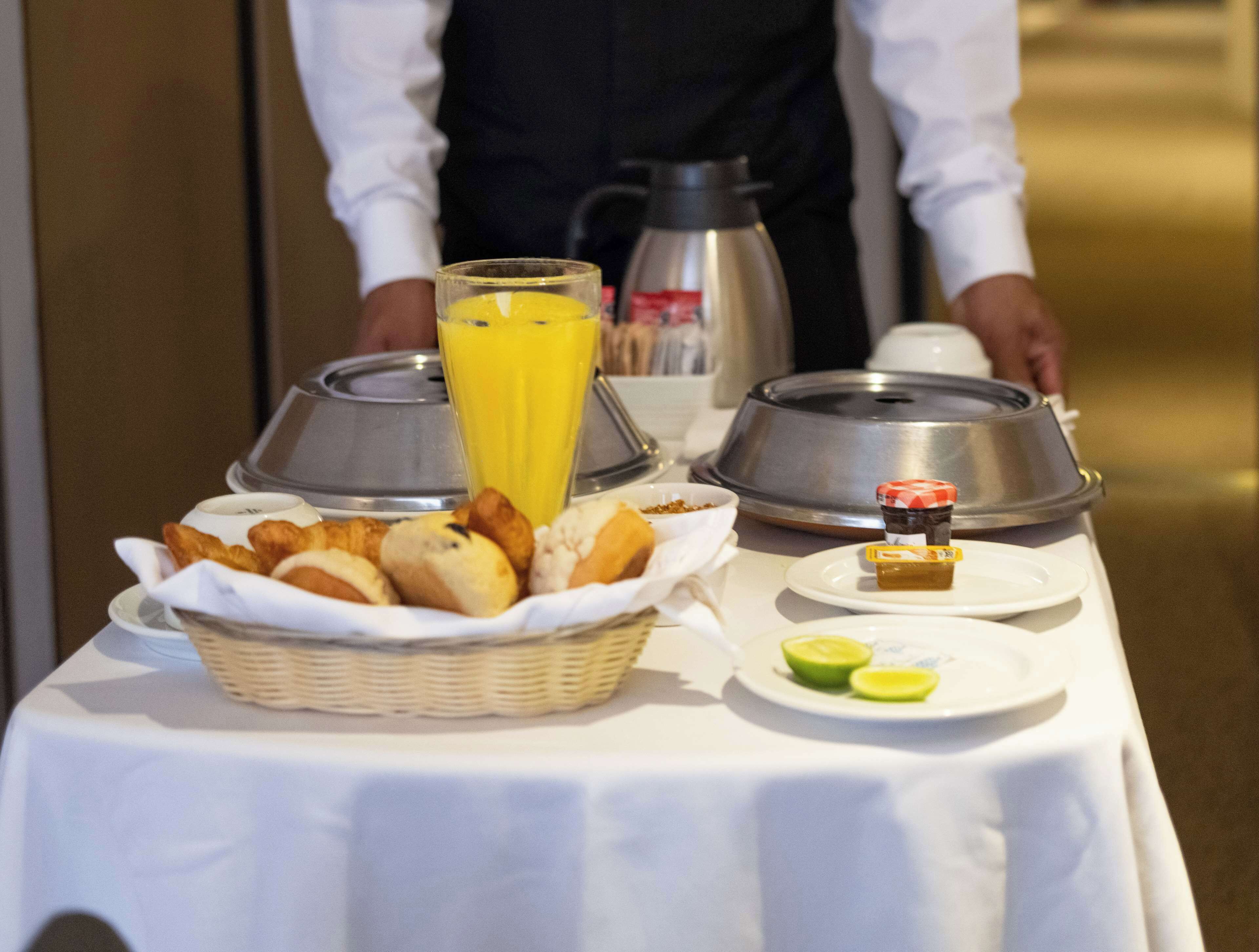 Ein Frühstücksbuffet mit verschiedenen Backwaren, einem Glas Orangensaft und einer Kaffeekanne auf einem Tisch.