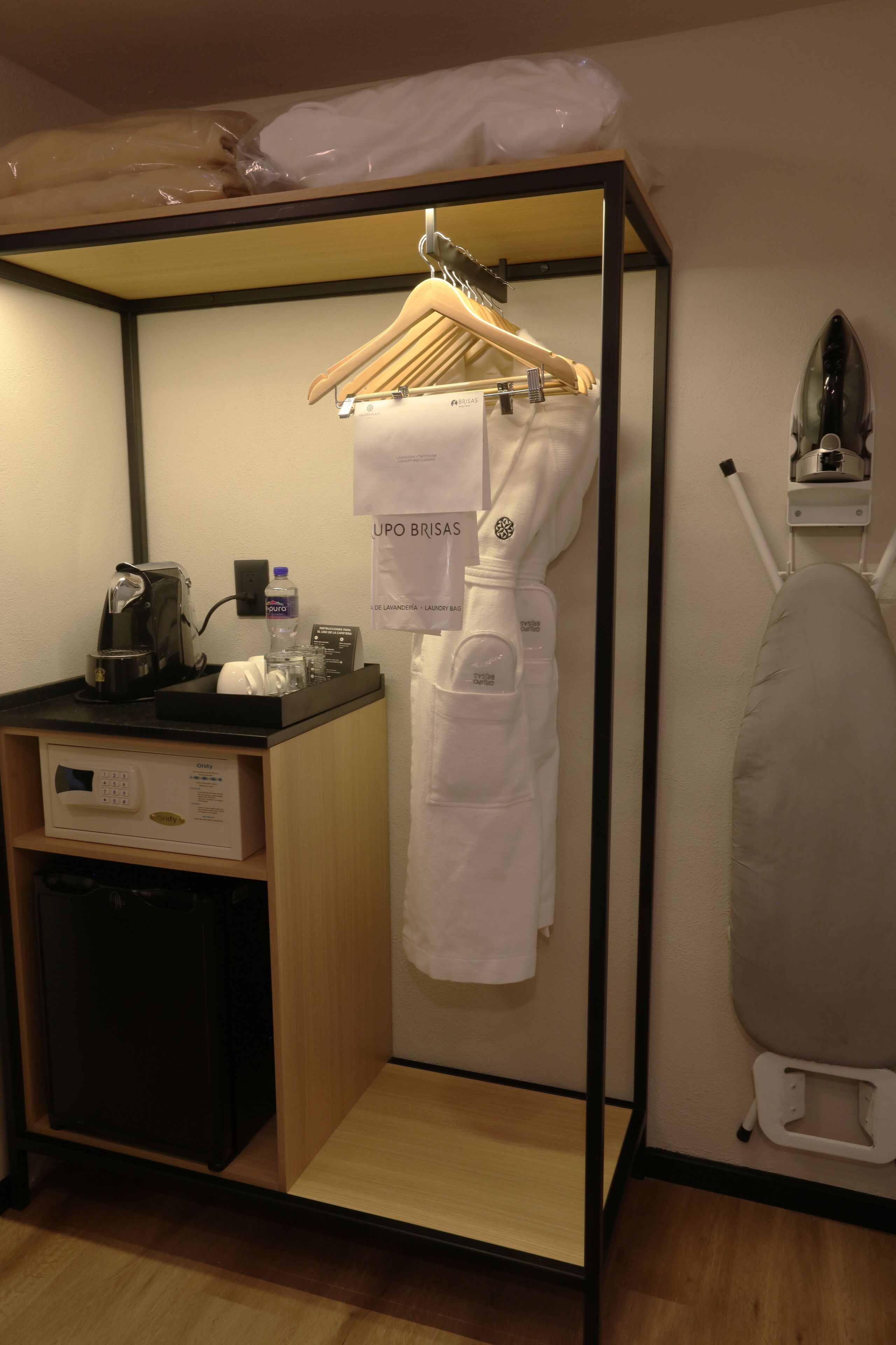 Une chambre d’hôtel compacte équipée d’une kitchenette, d’un sac à linge suspendu, d’une machine à café et d’un fer à repasser portatif.