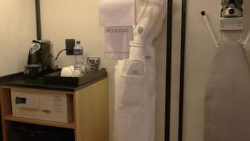 Habitación de hotel compacta con kitchenette, una bolsa para ropa colgada, una cafetera y un planchador portátil.