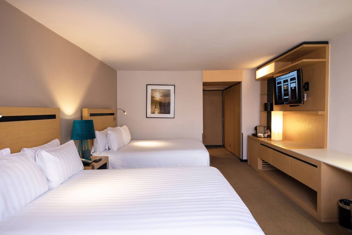 A hotel room with two beds, a desk, a TV, and a framed picture on the wall.