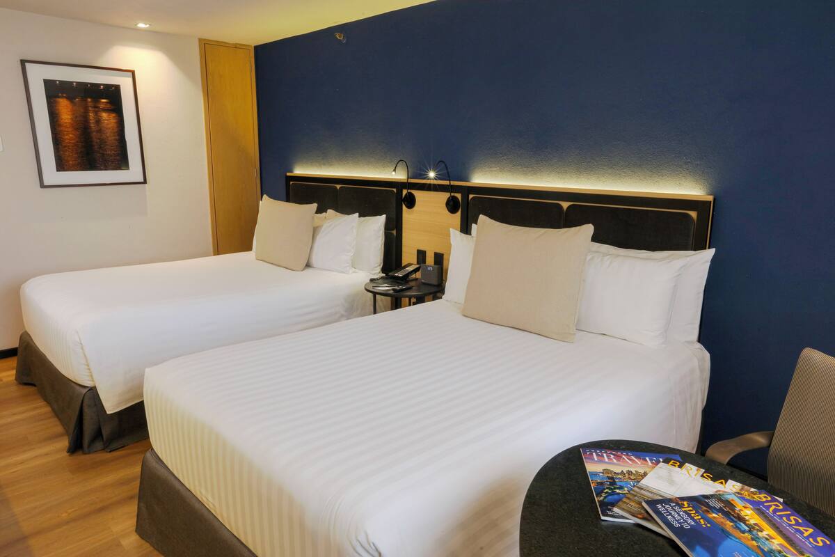 A hotel room with two beds, a nightstand, and a magazine on the table.