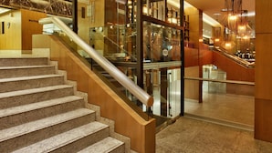 A modern hotel lobby with a marble staircase, glass railings, and contemporary lighting fixtures.