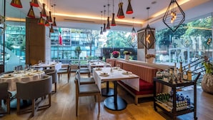 A restaurant with wooden flooring, tables set with white tablecloths, and hanging pendant lights.
