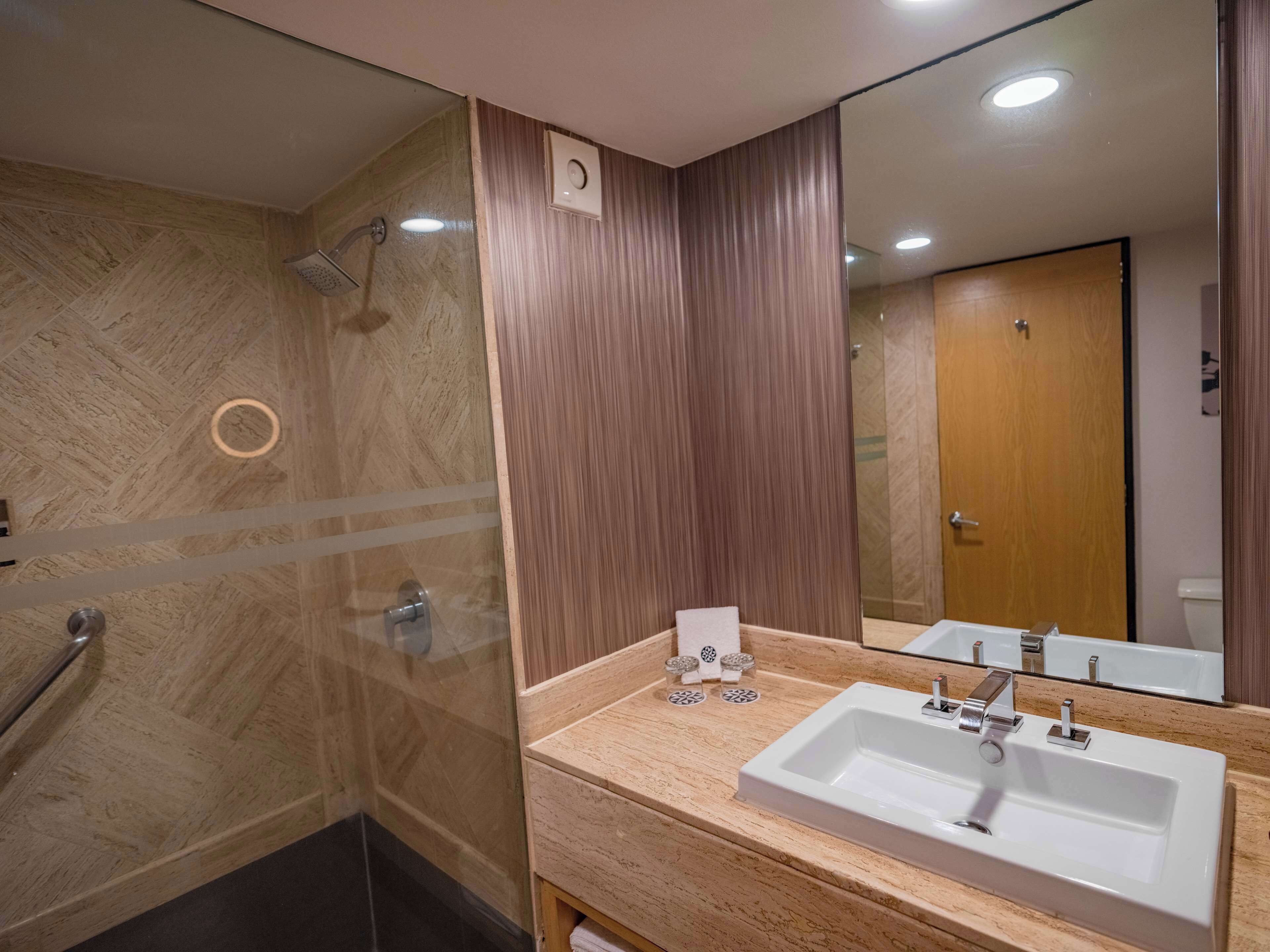 A modern bathroom with a large mirror, a sink, and a shower.