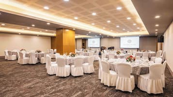 Uma sala de conferências com mesas redondas, cadeiras brancas e centros de mesa com flores.
