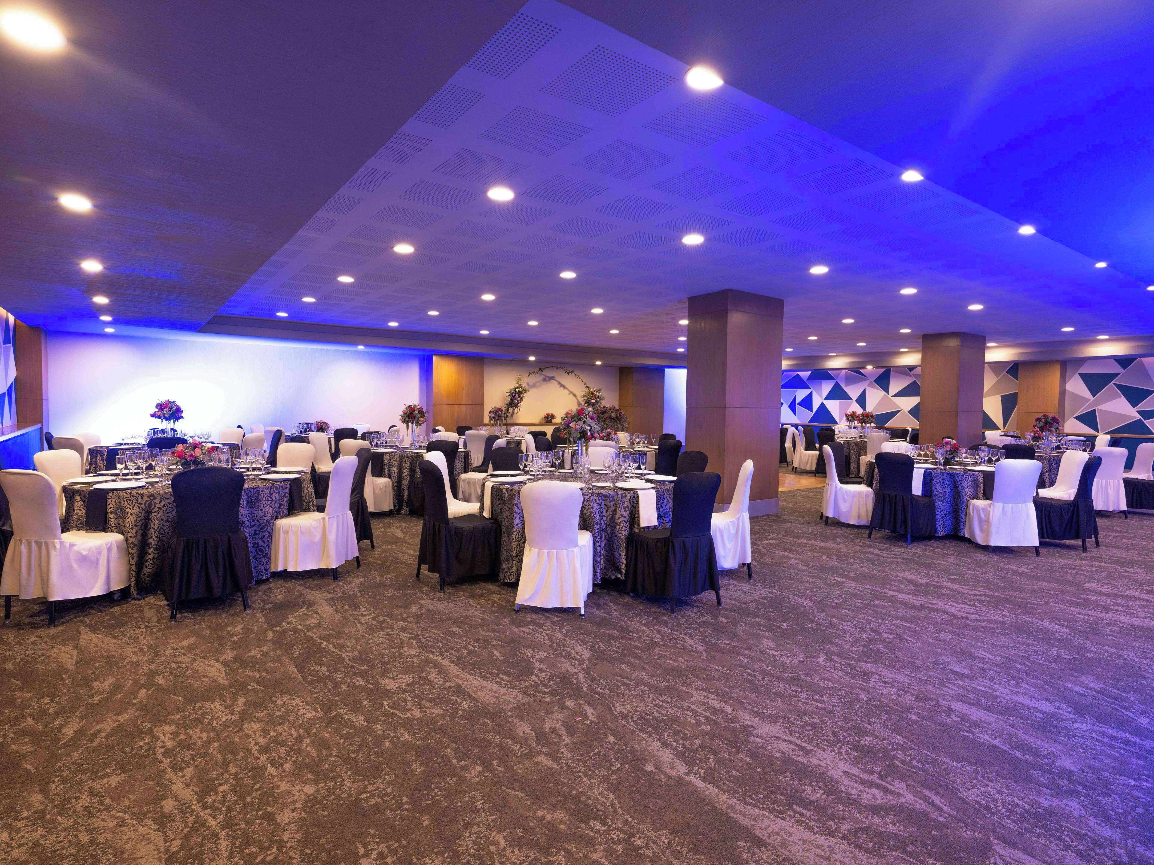 A banquet hall with round tables, chairs, and a carpeted floor.
