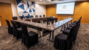 A conference room with a long table, chairs, water bottles, and a projector screen displaying "GALERÍA PLAZA REFORMA".