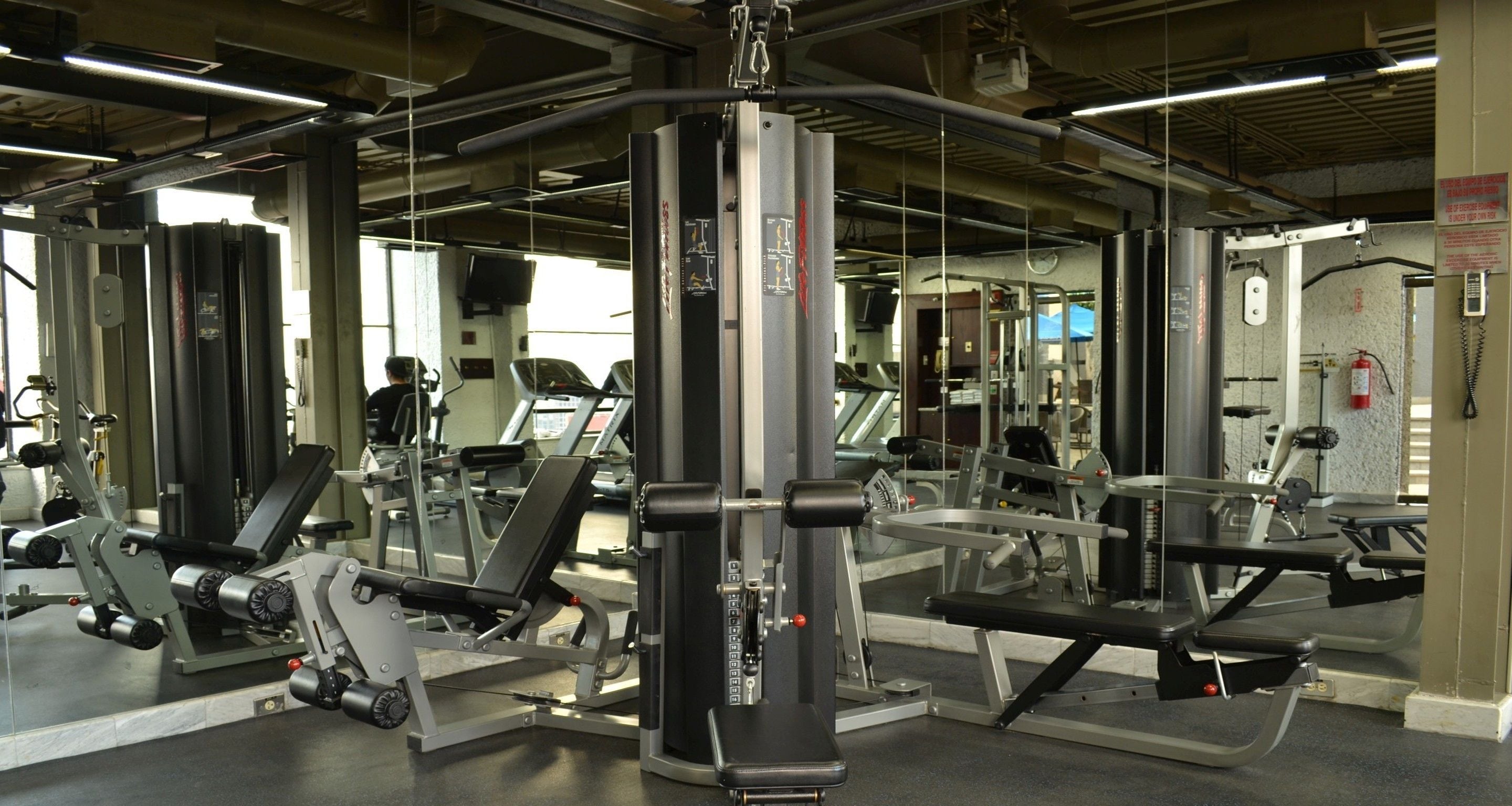 Una palestra con diverse macchine per esercizi, specchi e un estintore a parete.