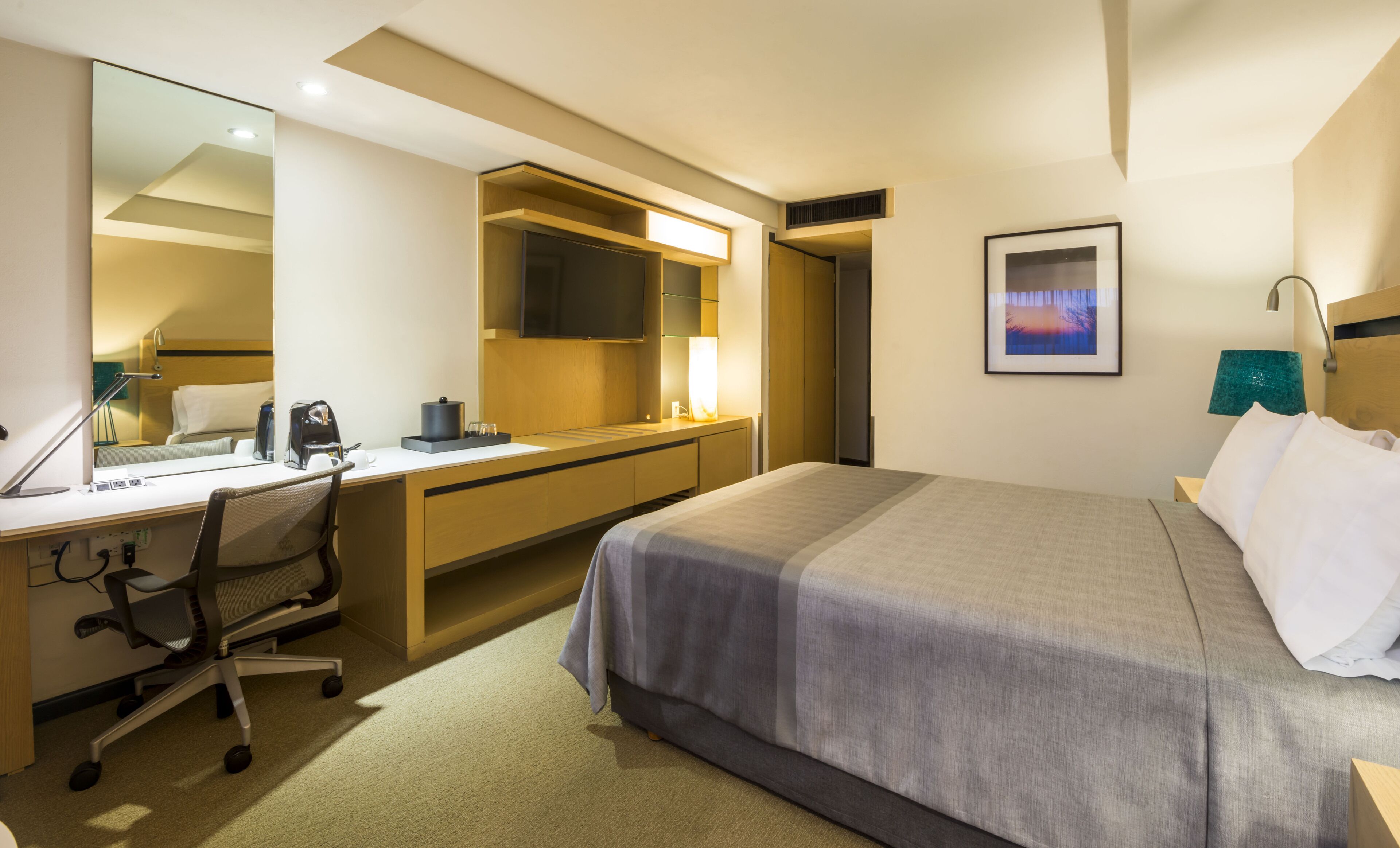 A hotel room with a bed, desk, chair, and a TV mounted on the wall.