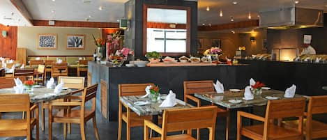 Een restaurant met houten tafels en stoelen, een bar in het midden en kunstwerken aan de muren.