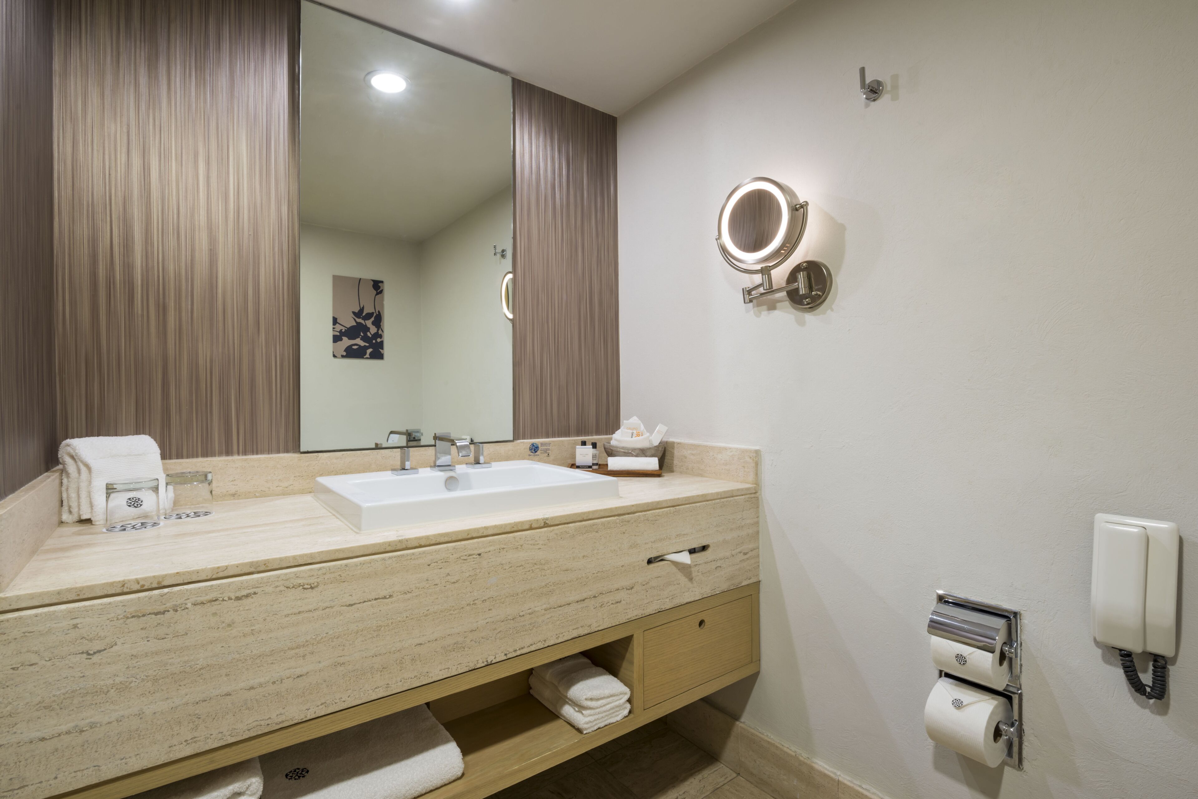 A bathroom with a double sink, a mirror, a towel rack, a toilet paper holder, and a phone.