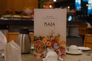 Un ambiente de desayuno con una pizarra de menú, una cafetera, un hervidor de té y comida para el desayuno sobre la mesa.