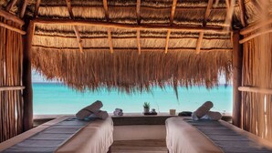 Una habitación con dos camas, techo de paja y vista al océano.