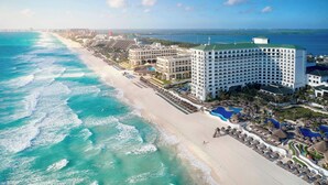 Un hotel frente a la playa con varias construcciones, una playa de arena y una vista despejada del océano.