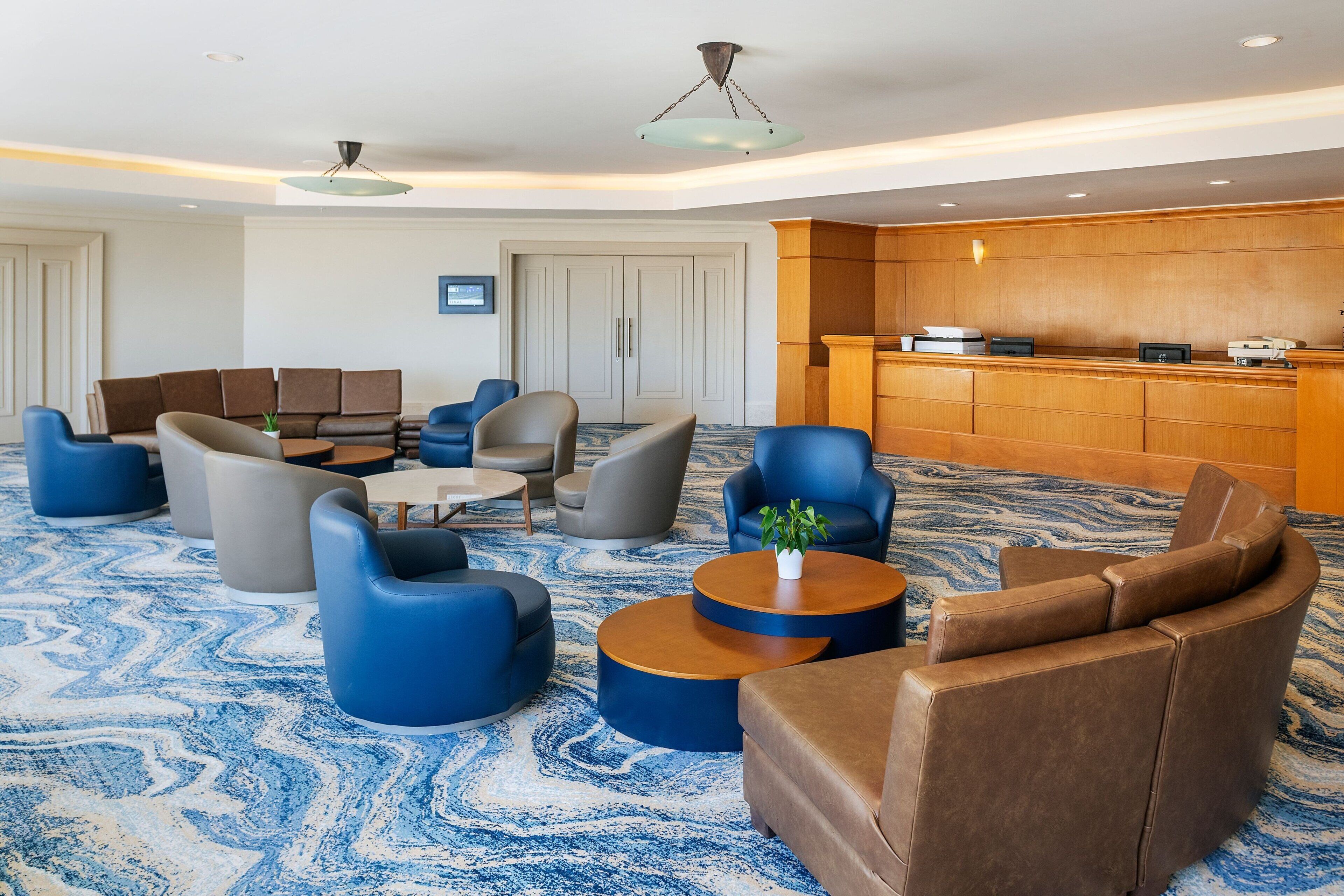 Eine Lobby mit blauen und braunen Sitzgelegenheiten, einem Empfangstresen und einem gemusterten Teppich.