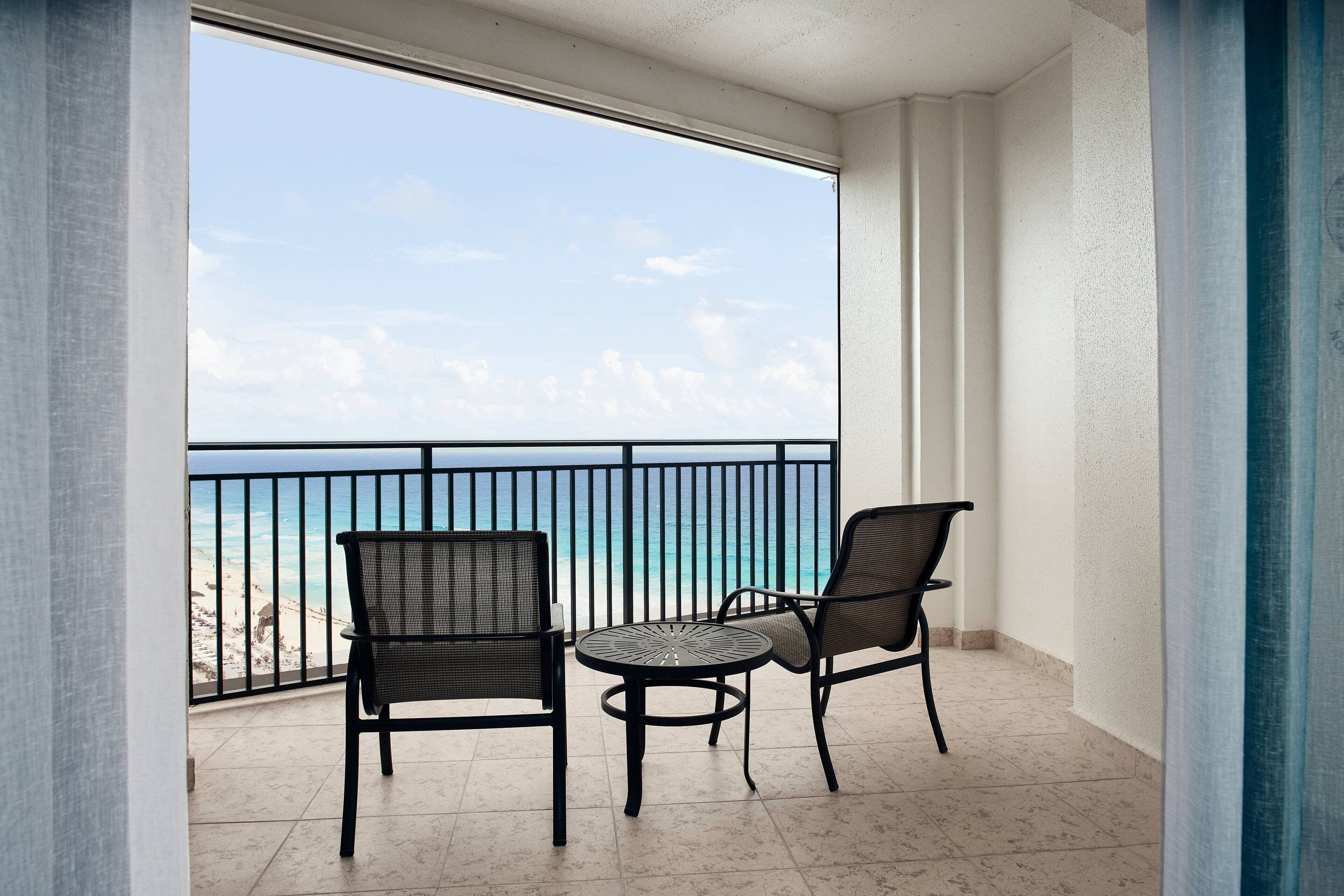 Varanda com duas cadeiras e uma mesa pequena, com vista para a praia e o oceano.