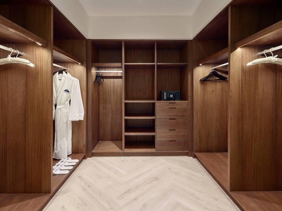 A walk-in closet with wooden shelving, a white robe, and a black box on the shelves.