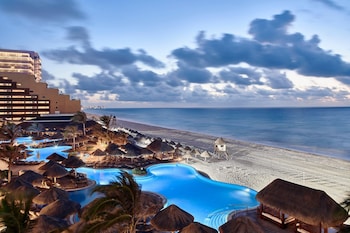 An indoor dining area with wooden tables and chairs, a thatched roof, and a view of the ocean. at JW Marriott Cancun Resort & Spa