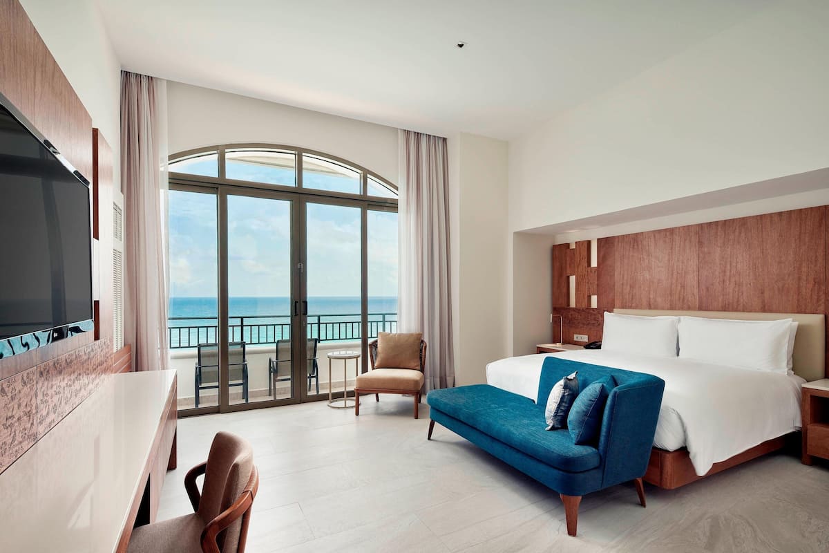 A hotel room with a large bed, a sofa, a TV, and a balcony with a view of the sea.