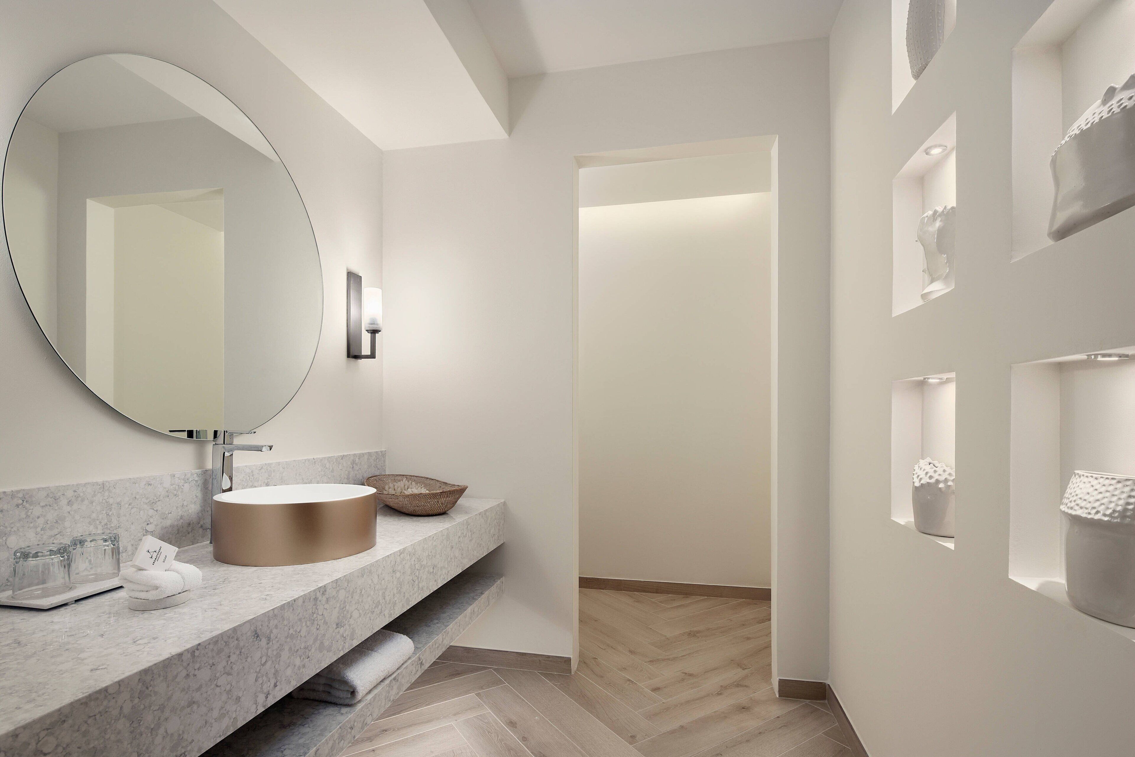 A modern bathroom with a large mirror, a round sink, and a marble countertop.