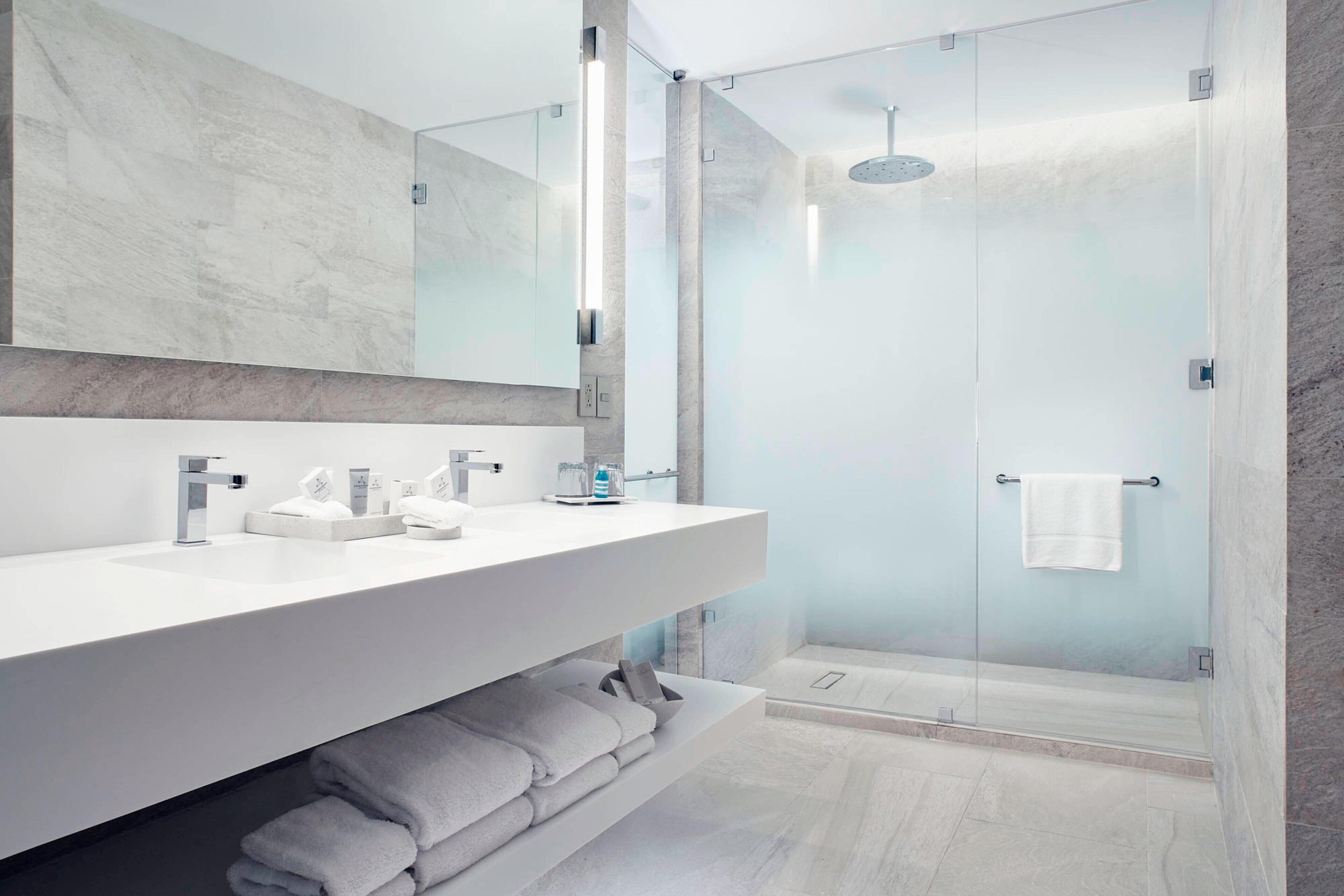 A modern bathroom with a large mirror, two sinks, and a glass-enclosed shower.