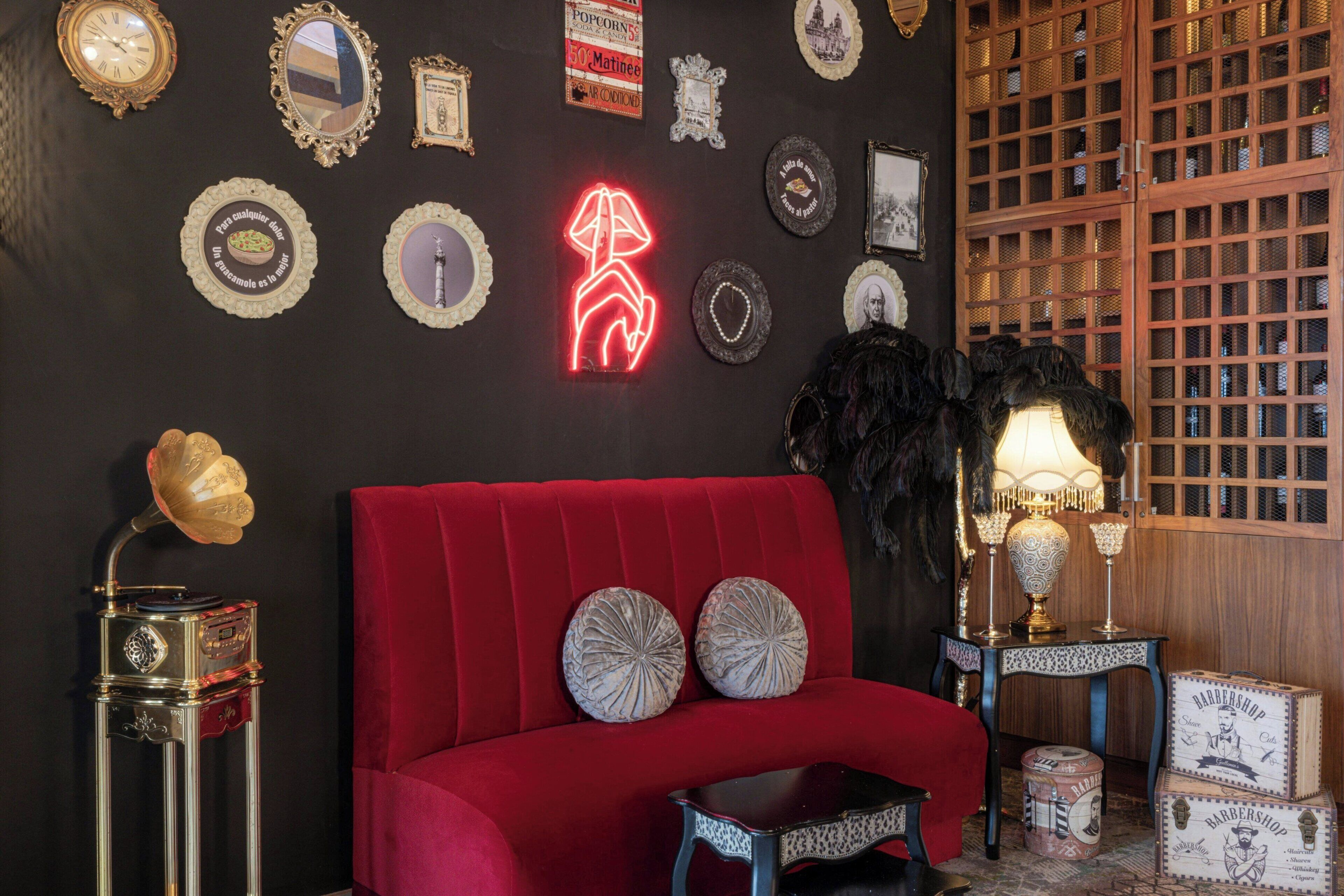 Een rode bank met decoratieve kussens, een vintage gramofoon en een neonbord met een hond erop.