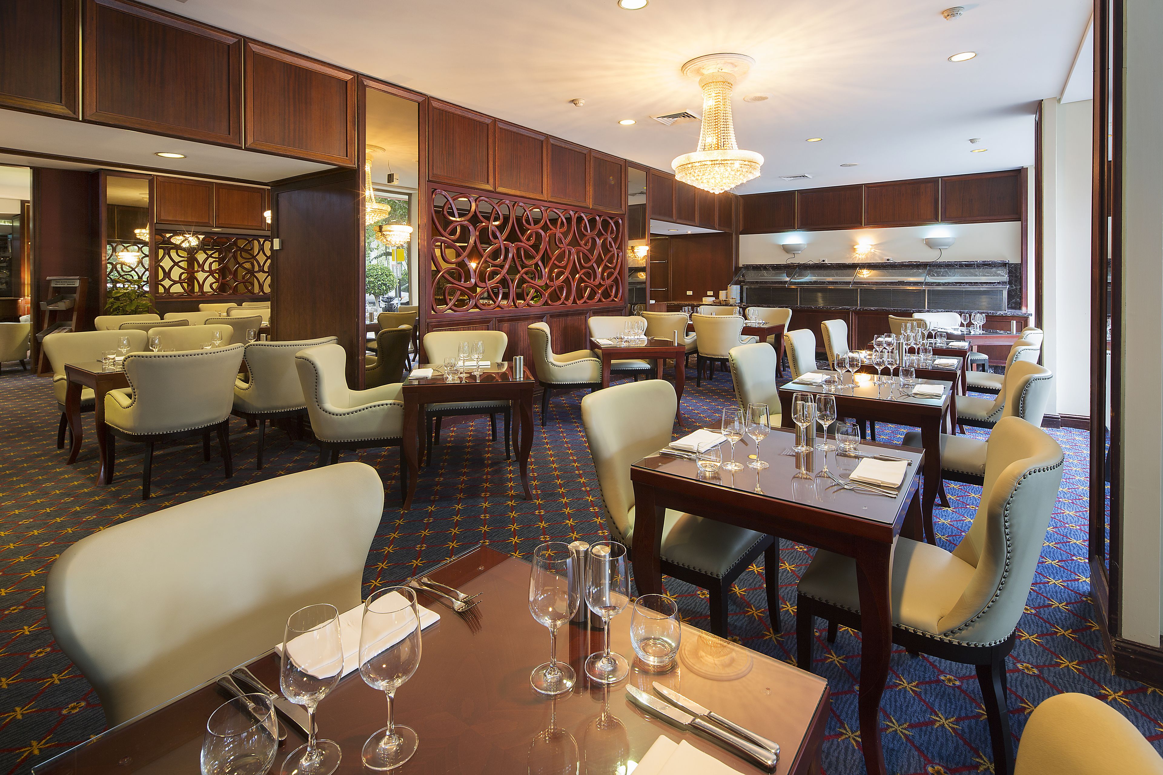 A hotel dining area with multiple tables and chairs, a decorative wall, and a chandelier.