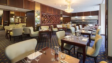A hotel dining area with multiple tables and chairs, a decorative wall, and a chandelier.