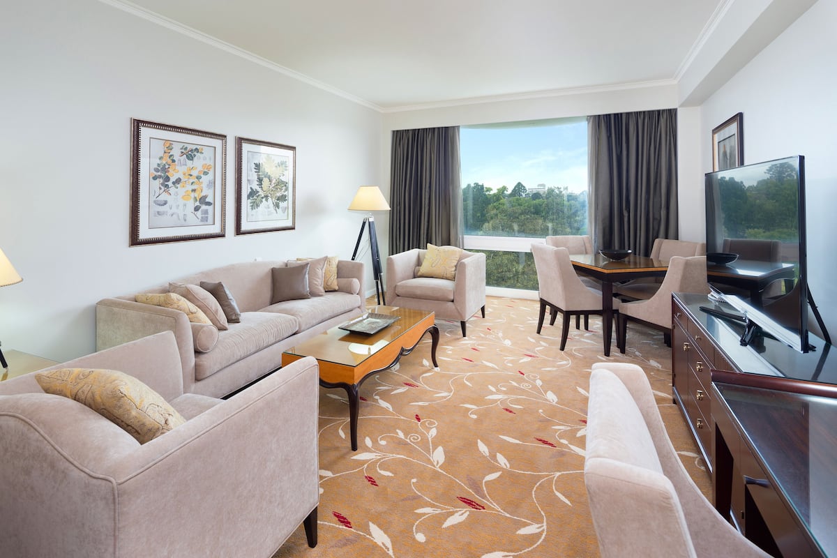 A hotel room with a sofa set, a dining table with chairs, a TV, and artwork on the walls.