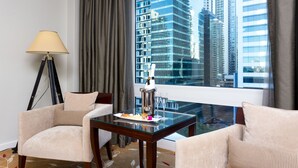 Habitación de hotel con una mesa de vidrio, dos sillones, una lámpara y vistas a edificios altos.