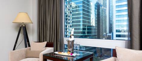 A hotel room with a glass table, two armchairs, a lamp, and a view of tall buildings.