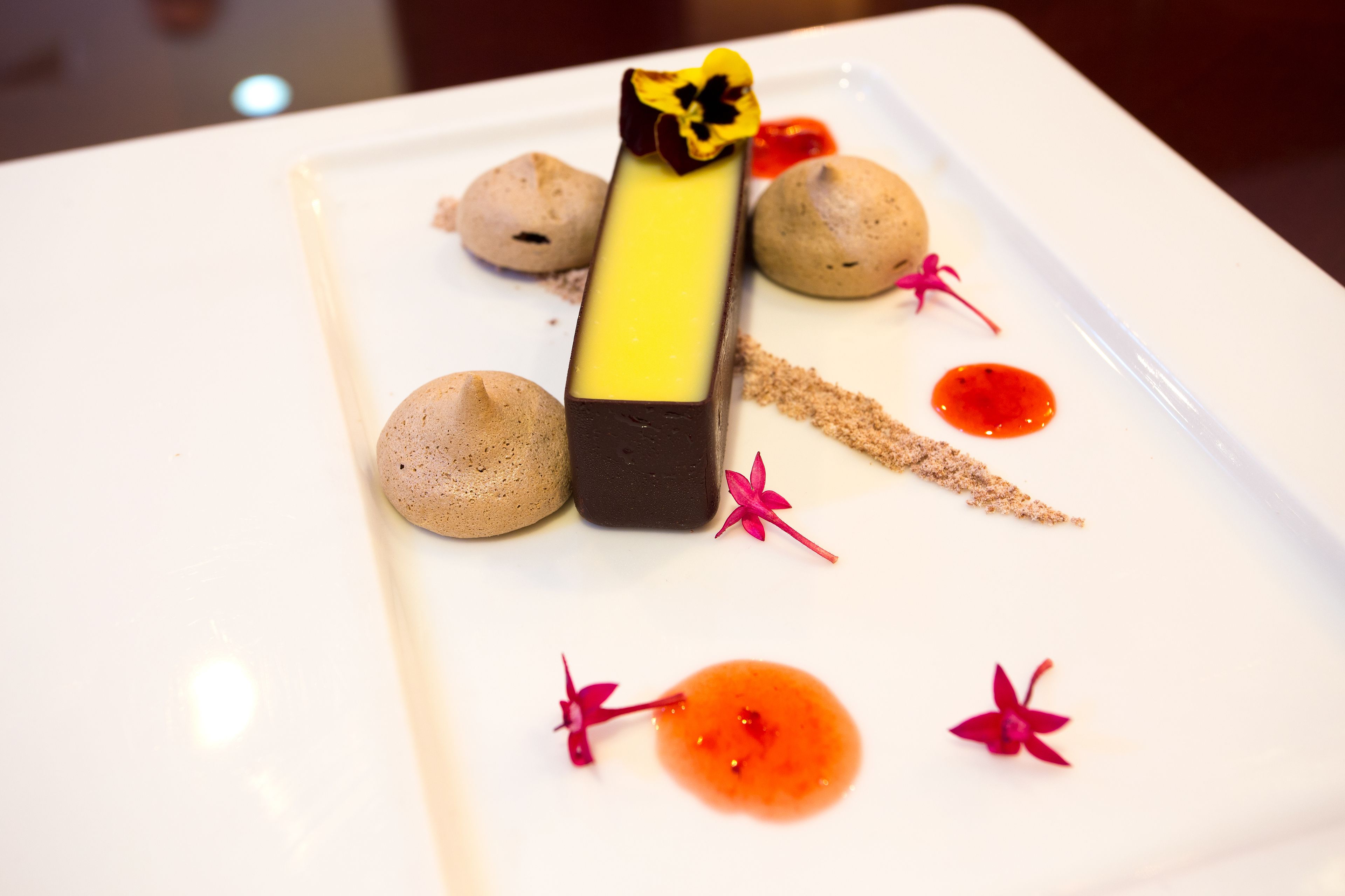 A dessert plate with a rectangular chocolate piece, spherical meringues, and red sauce with flower decorations.