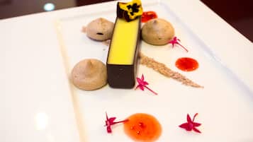 A dessert plate with a rectangular chocolate piece, spherical meringues, and red sauce with flower decorations.