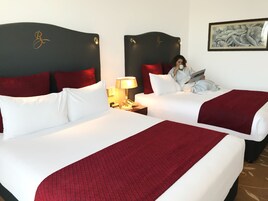 A hotel room with two beds, red and white bedding, a nightstand with a lamp, and a framed picture on the wall.