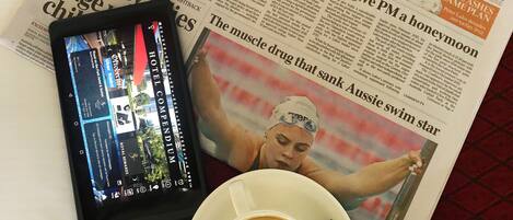 A newspaper, a tablet, a cup of coffee, and a packet of snacks on a table.