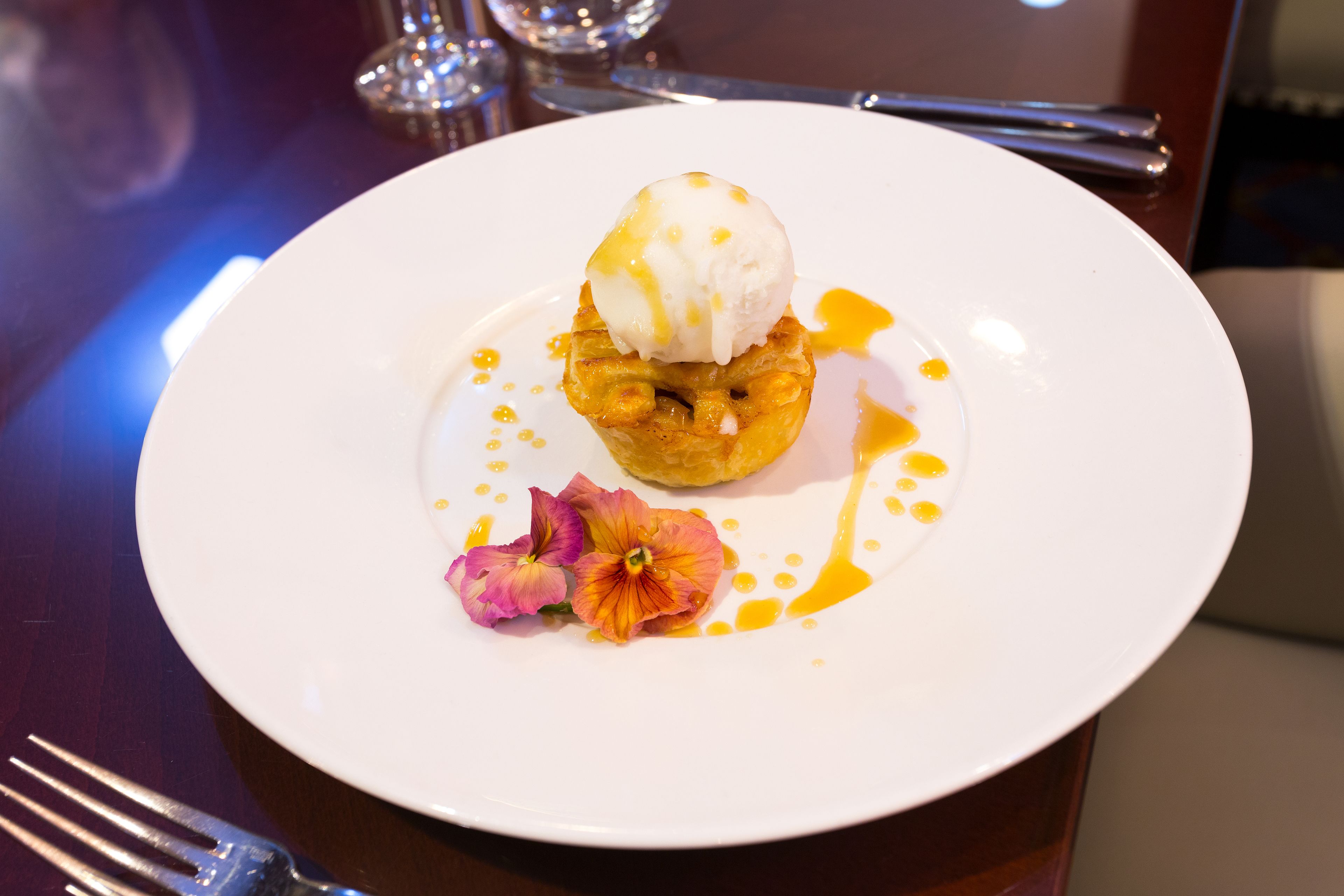 Un plato de postre con una porción de helado sobre un pastel, acompañado de una flor y cubierto con jarabe.