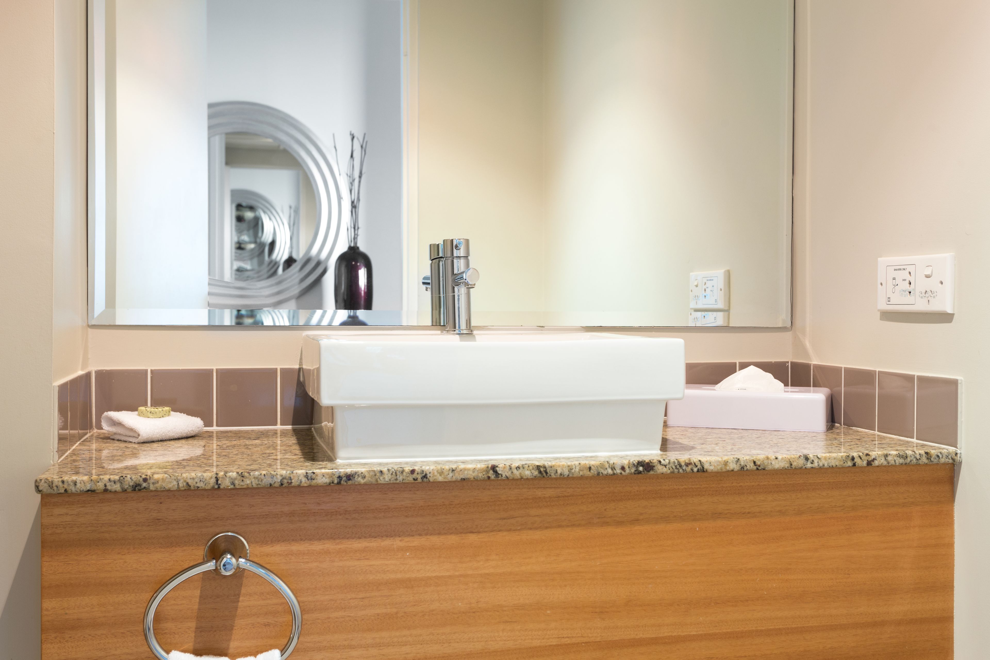 A modern bathroom with a large mirror, a white sink, and a granite countertop.