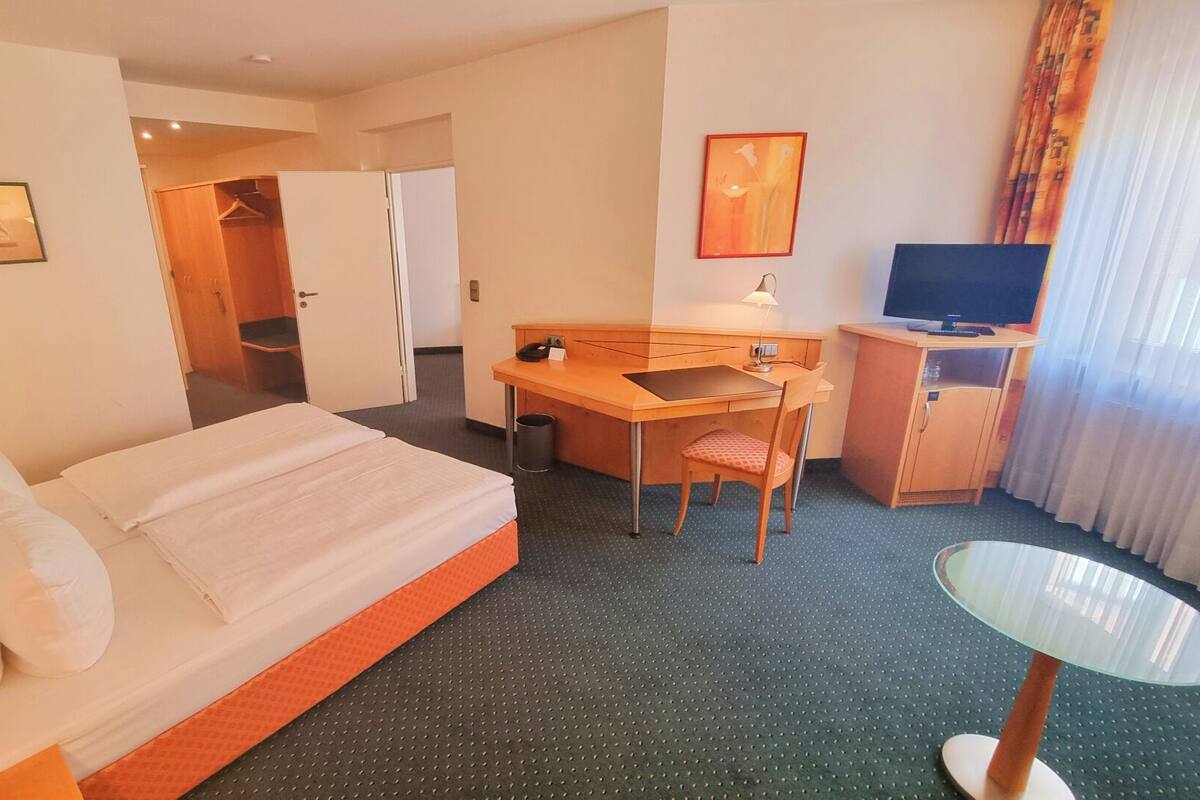 Ein Hotelzimmer mit Bett, Schreibtisch, Stuhl, Fernseher und einem kleinen Tisch.