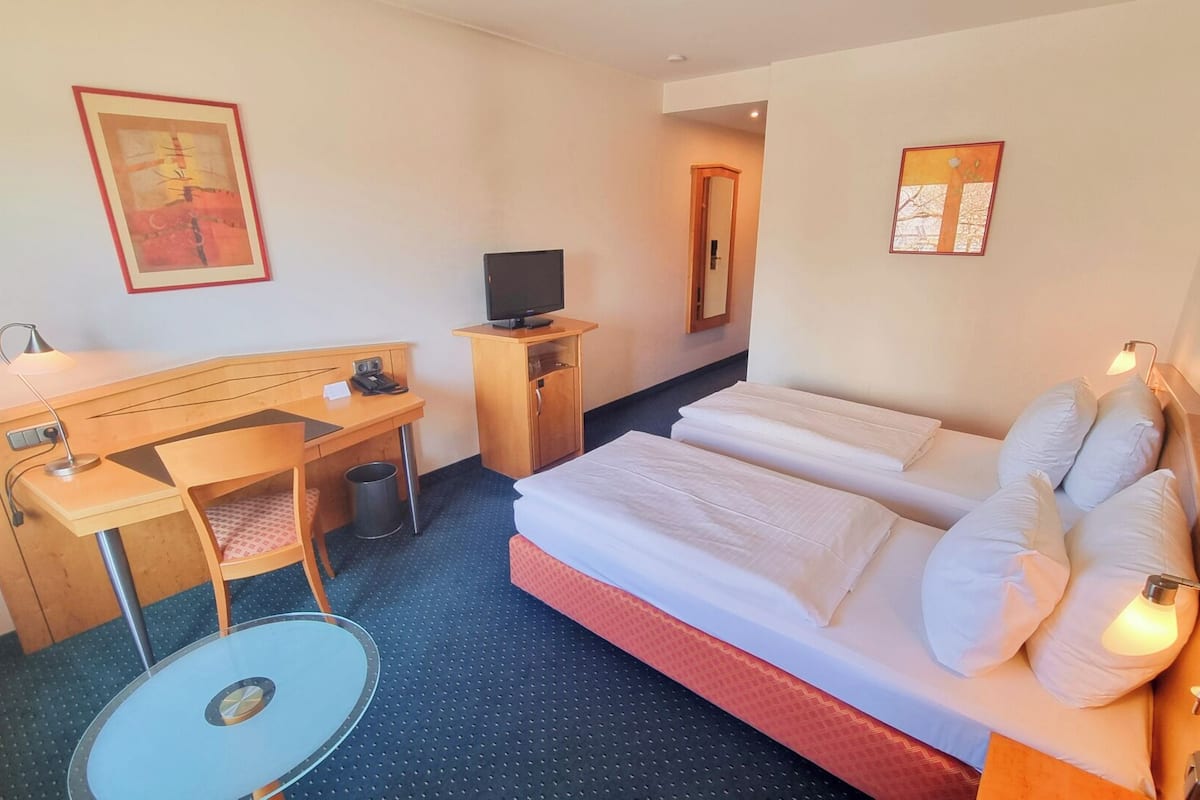 Ein Hotelzimmer mit Bett, Schreibtisch, Stuhl, Fernseher und einem kleinen Tisch.