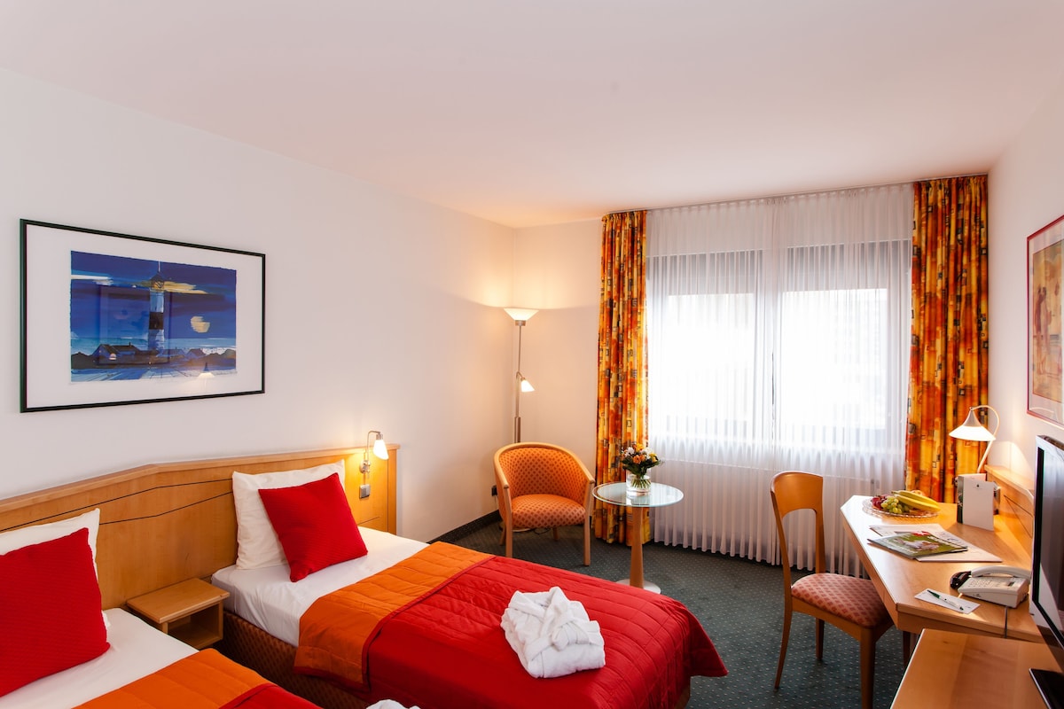 Een hotelkamer met twee bedden, een bureau, een stoel, een lamp en een schilderij aan de muur.