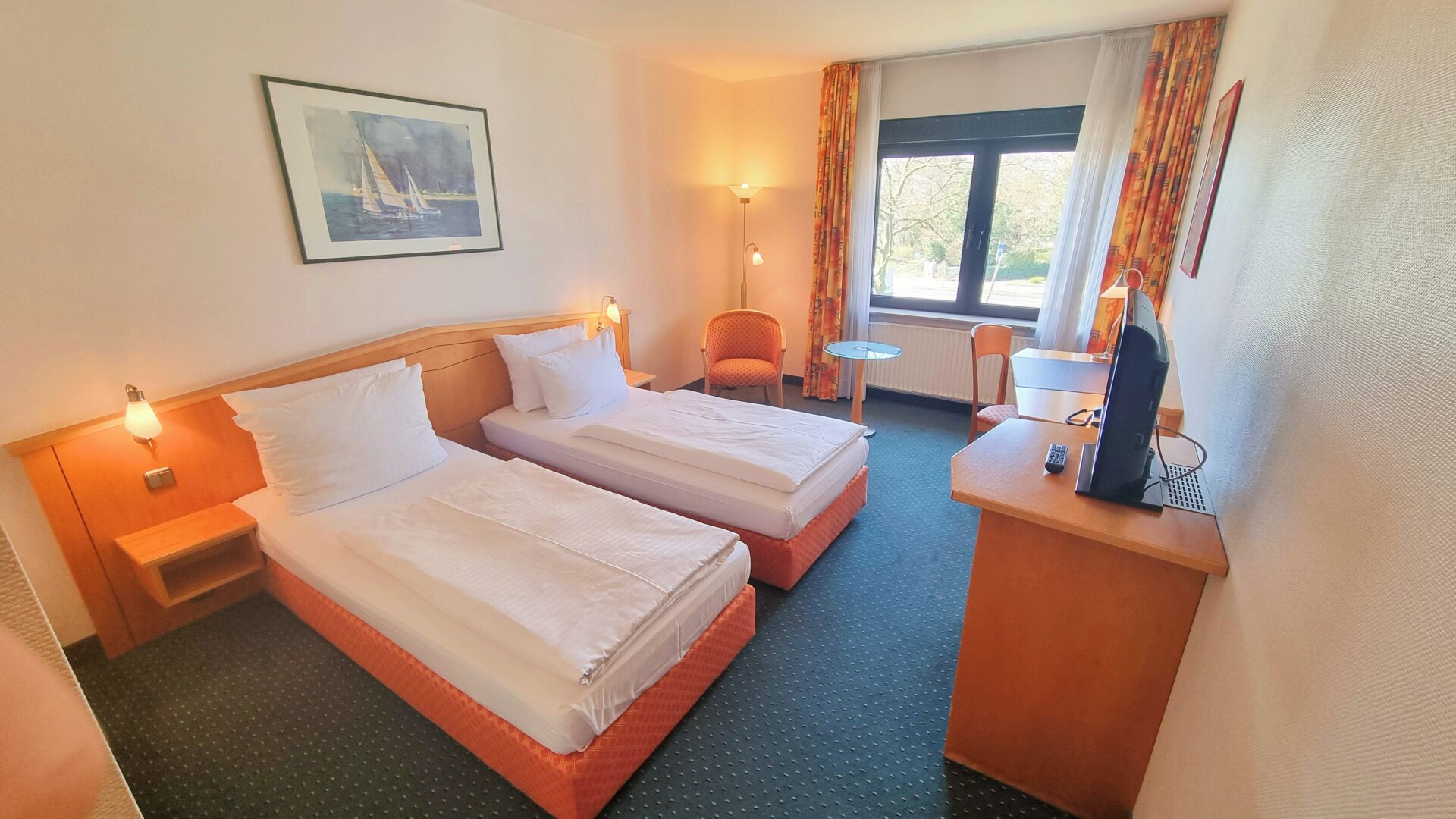A hotel room with two beds, a desk with a computer, a chair, and a window with curtains.