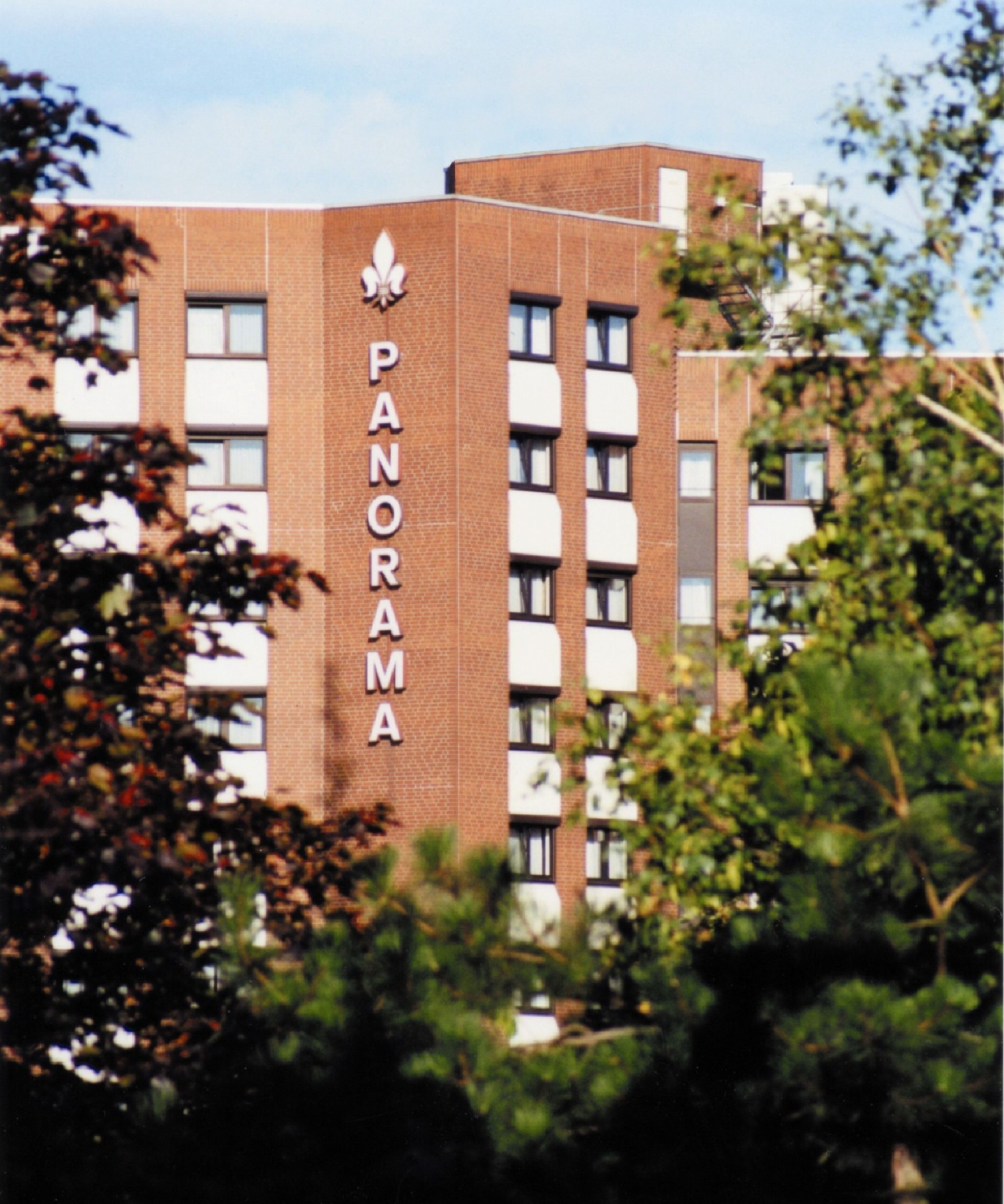A multi-story building with the name "PANORAMA" on its facade, surrounded by greenery.