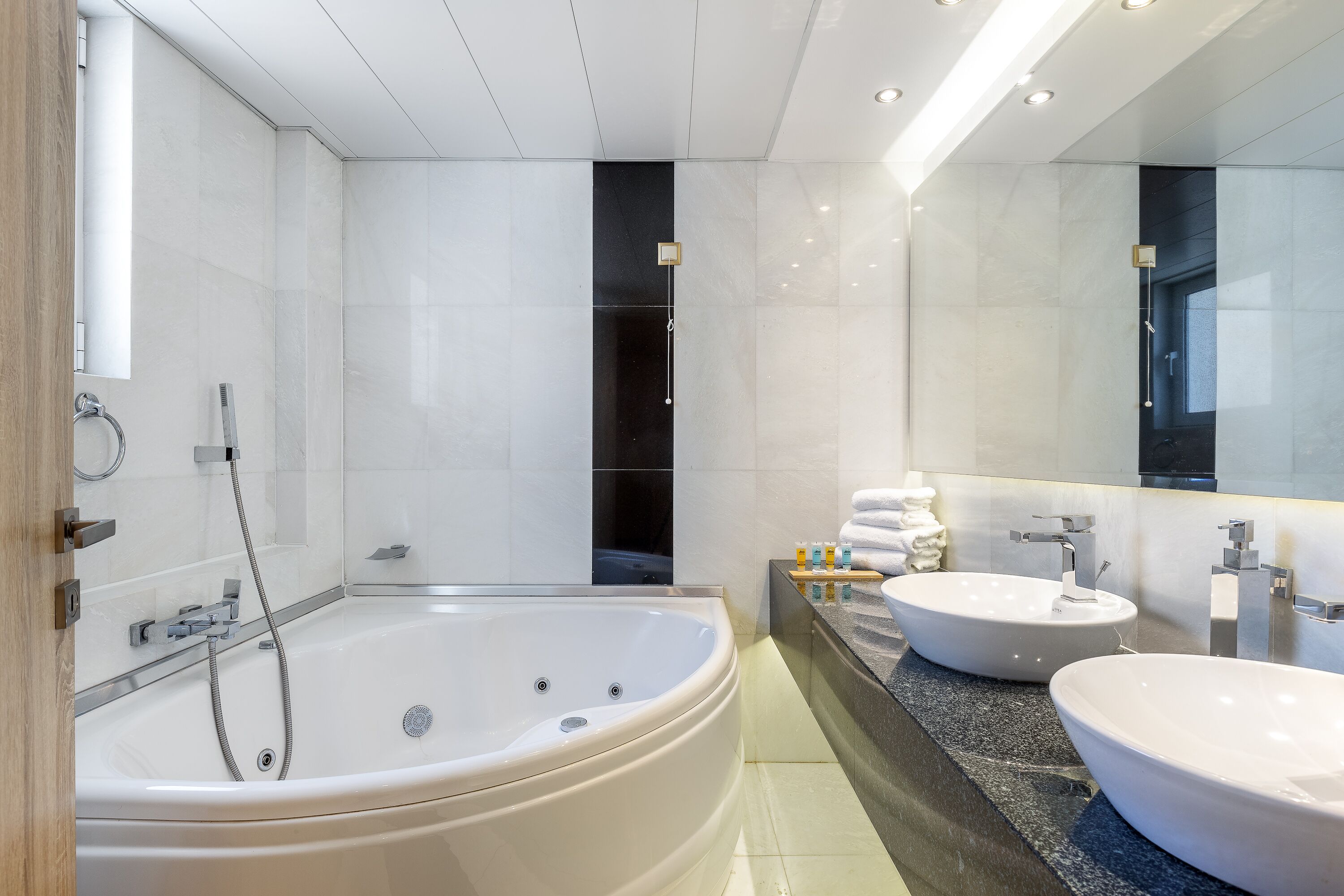 A modern bathroom with a large freestanding bathtub, two sinks, and a large mirror.