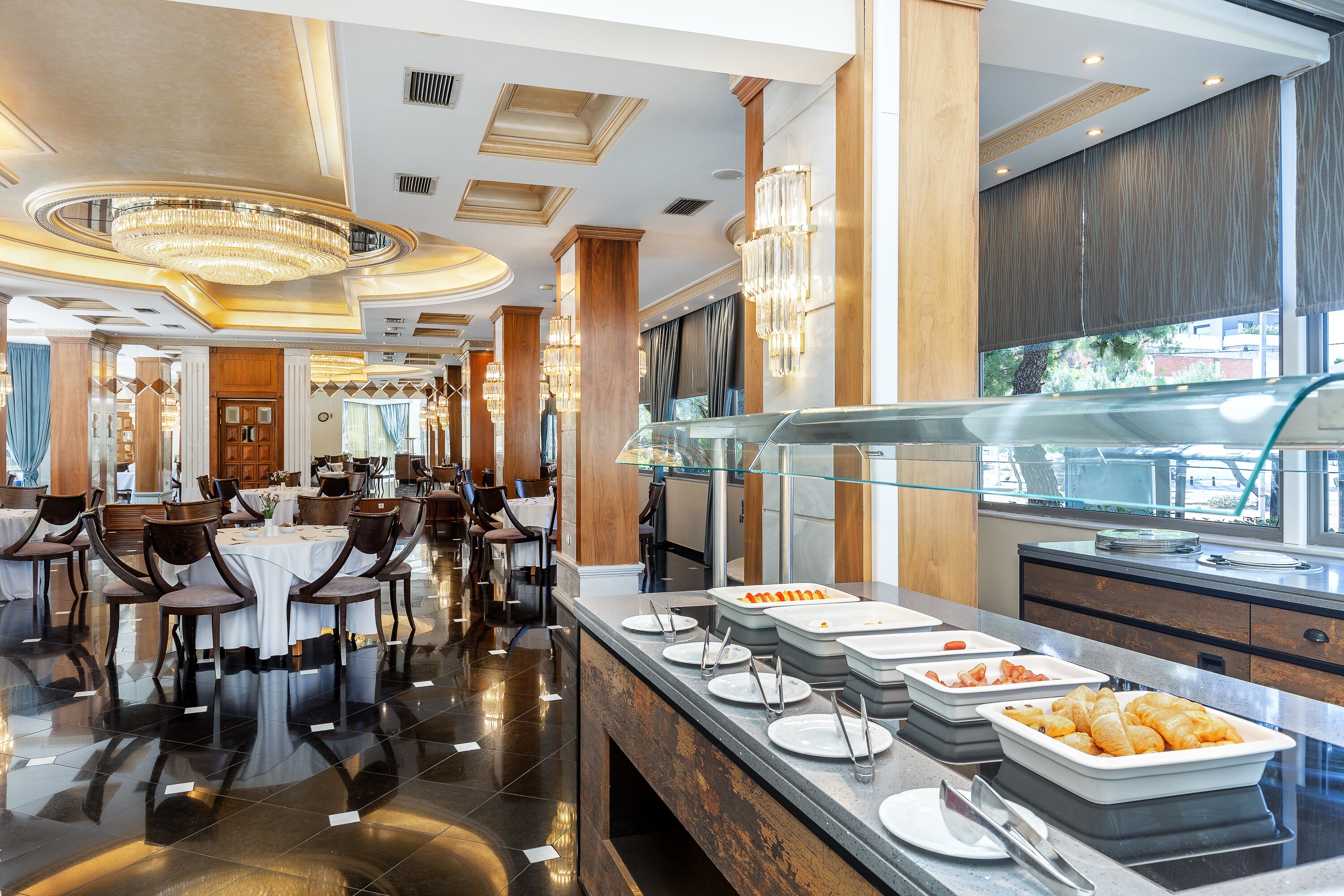 Un espace de restauration moderne dans un hôtel, avec un buffet, des sols cirés et d’élégants lustres.