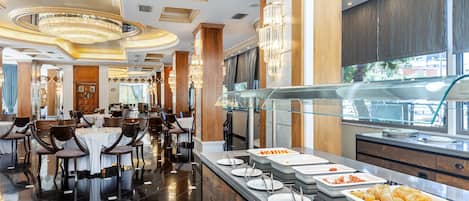 A modern hotel dining area with a buffet setup, polished floors, and elegant chandeliers.