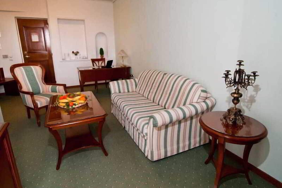 A living room with a striped sofa, a dining table with fruit, a chair, a small side table, and a chandelier.