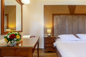 Habitación de hotel con cabecera de madera, mesita de noche con lámpara, espejo y cama con ropa blanca.